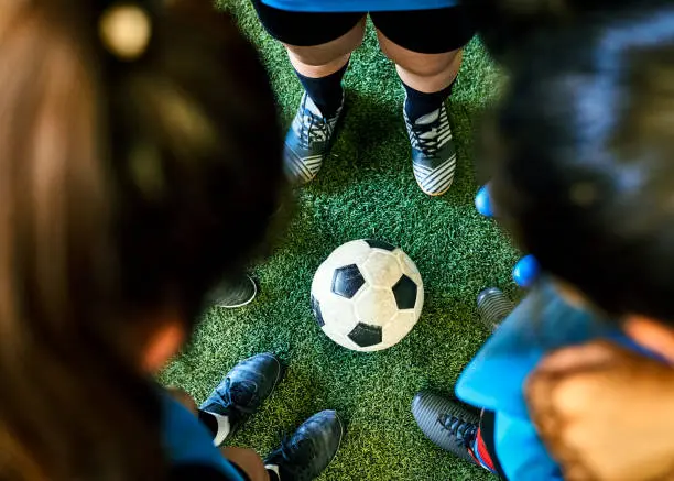 High angle view of a girls team in huddle at sports court with soccer ball in ground. Female players huddling at indoor soccer court.