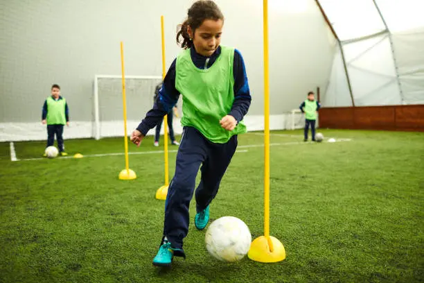 Group of children on soccer training. Kicks soccer ball around yellow cones.